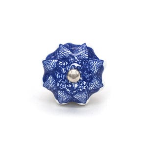 May include: A blue and white ceramic cabinet knob with a starburst design. The knob features a silver metal center and a textured pattern. The decorative hardware is suitable for drawers and cabinets.