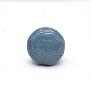 May include: A light blue ceramic knob with a crackled glaze finish. The knob is round and has a slightly irregular shape.