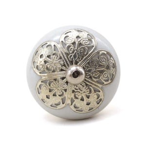 May include: White ceramic cabinet knob with a silver filigree design in the shape of a flower.