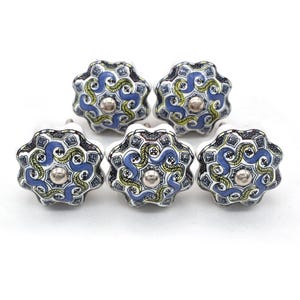 May include: A collection of five ceramic cabinet knobs. Each knob features a floral design with blue, yellow, and white patterns. The knobs have a silver-colored metal center and are set against a white background.