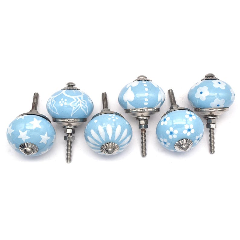 Hand-painted sky-blue ceramic knobs with assorted white designs (stars, flowers, stripes) for cabinets and drawers.