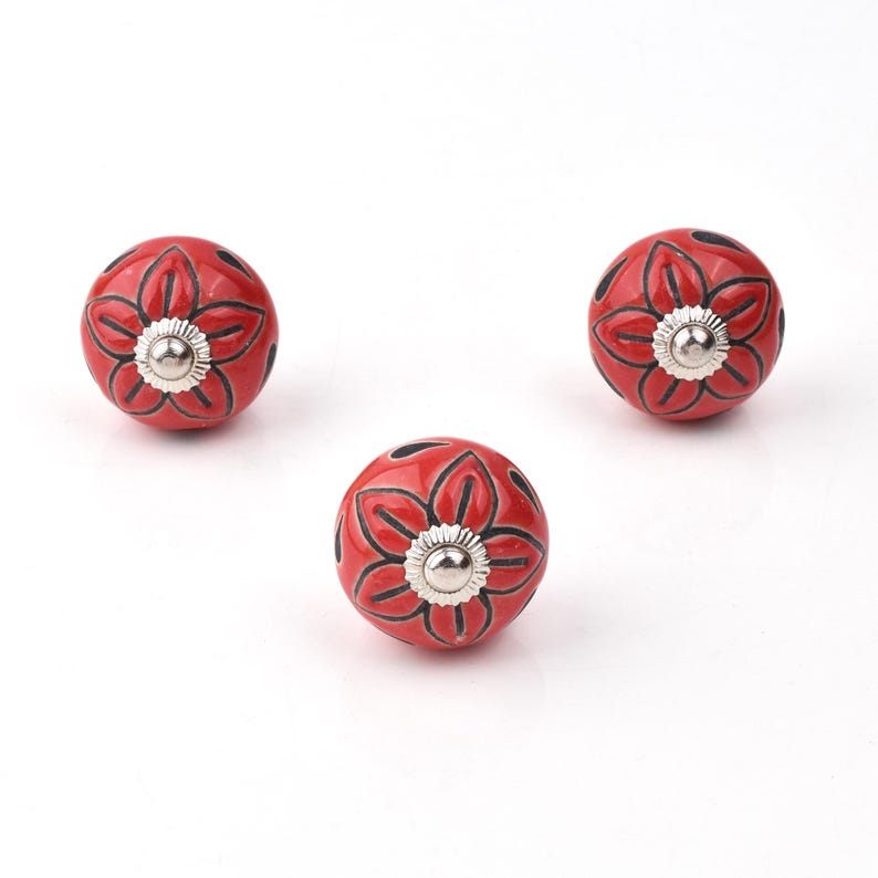 Red ceramic knobs with hand-painted white floral and mandala designs; assorted cabinet knobs for furniture and home décor.