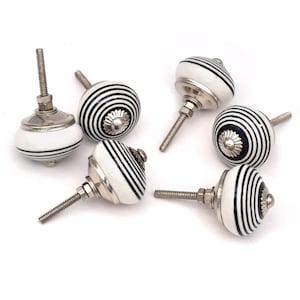 May include: Six white ceramic cabinet knobs with black stripes. Each knob has a silver screw.