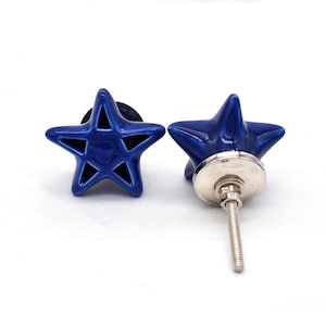 May include: Two cobalt blue star-shaped cabinet knobs. Each knob has a five-pointed star design with cut-out sections. The knobs have a glossy finish and are mounted on a silver-colored metal base with a threaded screw for installation. Decorative hardware.