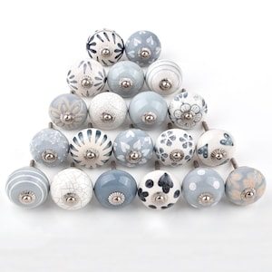 Peut inclure: Ensemble de boutons de meubles décoratifs en céramique, aux motifs variés. Les boutons sont principalement blancs et bleus, avec des motifs rayés, floraux et abstraits. Chaque bouton est monté sur une base métallique argentée.