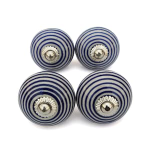 Puede incluir: Cuatro pomos redondos para armarios con base blanca y rayas azules concéntricas. Cada pomo tiene una base de metal plateado. Los pomos están dispuestos en forma cuadrada sobre un fondo blanco.