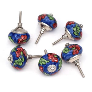 Może przedstawiać: Sześć niebieskich ceramicznych gałek do szafek z czerwonymi i zielonymi wzorami kwiatowymi oraz srebrnymi metalowymi podstawami i śrubami.