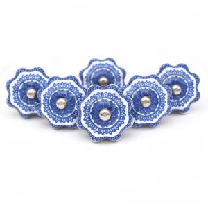 May include: Six blue and white ceramic drawer knobs with a floral design. The knobs have a silver center.