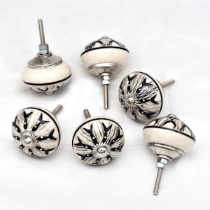 May include: Six white ceramic cabinet knobs with black and white geometric designs. Each knob has a silver screw.