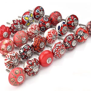 Red ceramic knobs with hand-painted white floral and mandala designs; assorted cabinet knobs for furniture and home décor.