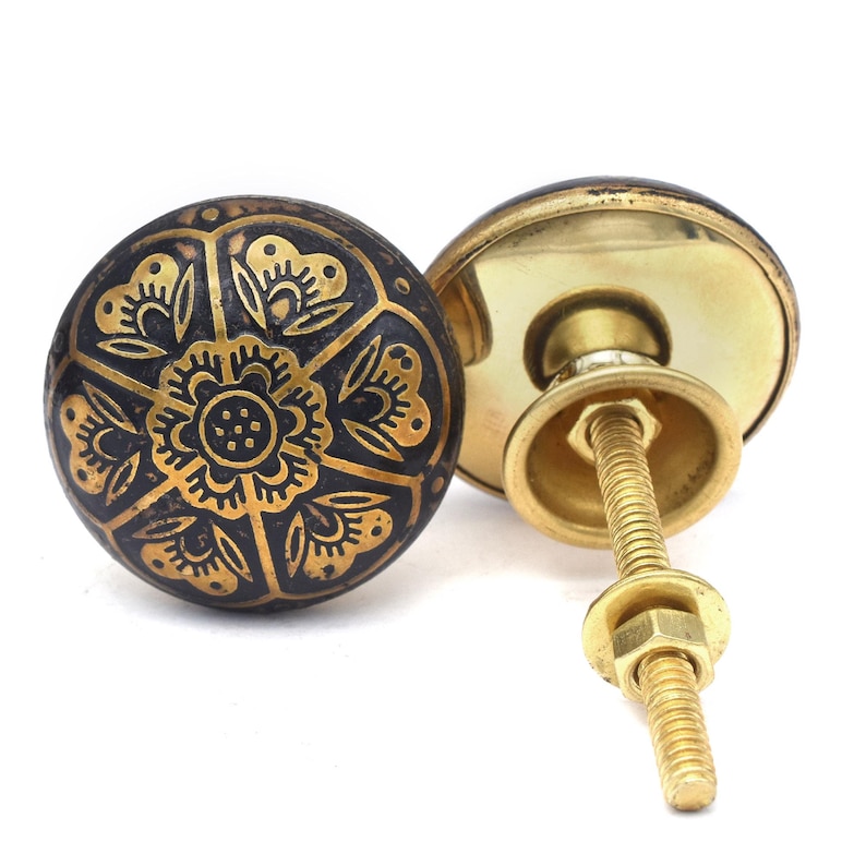 Etched brass flower cabinet knob with ornate gold pattern on dark background; decorative cabinet knobs for dresser hardware.