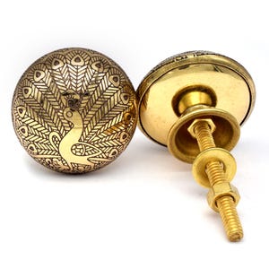 May include: Brass cabinet knob with a peacock design. The knob is round and has a screw on the back.