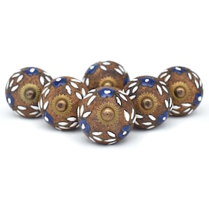 May include: A set of seven decorative cabinet knobs. Each knob is brown with a brass center and is decorated with white leaf-like patterns and blue floral accents. The knobs are arranged in a semi-circle.