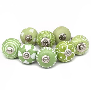 Könnte beinhalten: Satz von acht grünen Keramik-Schrankknöpfen mit weißen Blumen- und Herzmotiven. Jeder Knopf hat eine silberne Metallbasis.