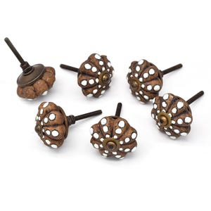 May include: Six brown ceramic cabinet knobs with white polka dots and a brass screw. The knobs have a flower-like design.