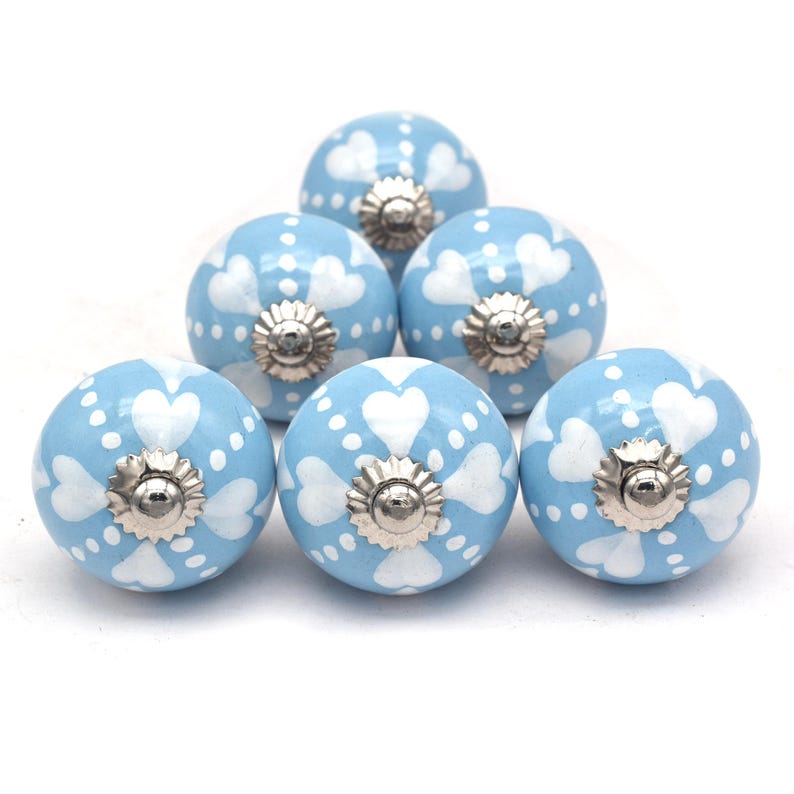 Six sky-blue ceramic knobs with white heart and dot patterns; cabinet and drawer knobs with metal screw centers.