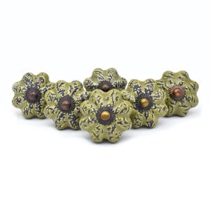 May include: Five green ceramic cabinet knobs with a textured surface and a gold center. The knobs have a distressed look and are shaped like a flower.