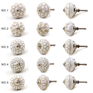 collection of white ceramic drawer knobs with intricate floral patterns and silver accents. The knobs are arranged in a basket lined with peach-colored fabric.