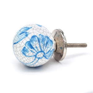 May include: A white ceramic knob with a blue floral design and a silver metal base. The knob has a crackled glaze finish.