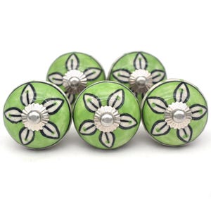 May include: Five green ceramic cabinet knobs with a floral design. Each knob features a light green base with a white and black floral pattern and a silver metal center. These decorative knobs are perfect for adding a touch of style to any cabinet or drawer.