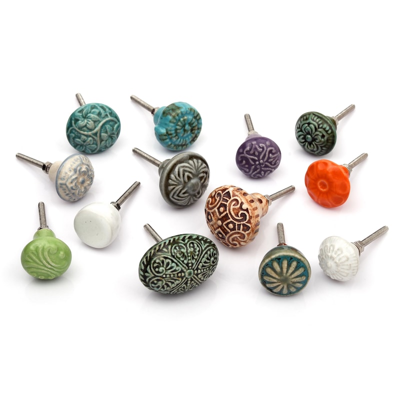 May include: A collection of twelve decorative cabinet knobs in various colours and patterns. Each knob features a round or oval shape with a metal bolt extending from the back. The designs include floral, geometric, and solid textures in shades of green, blue, orange, purple, white, and grey.