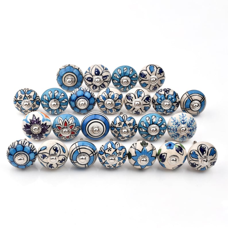 Assorted hand-painted ceramic knobs in blue, black and white with mandala and floral motifs for cupboard handles and kitchen decor.