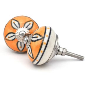 May include: Two ceramic cabinet knobs with a floral design. The knobs are orange with black and white accents. One knob has a silver screw.
