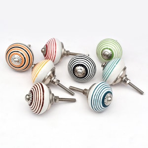 Könnte beinhalten: Eine Sammlung dekorativer Keramik-Schrankknöpfe mit verschiedenen Streifenmustern in Farben wie Orange, Schwarz, Rot, Gelb, Braun, Grün und Blau. Jeder Knopf hat eine silberfarbene Metallbasis und eine Schraube.