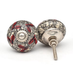 May include: Two ceramic cabinet knobs with a gray and white speckled background and red geometric patterns. The knobs have a silver metal base and screw.