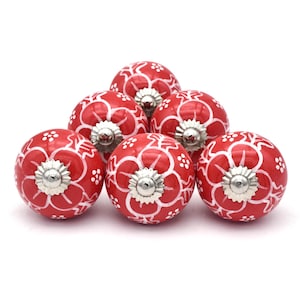 Könnte beinhalten: Sechs rote Keramik-Schrankknöpfe mit weißen Blumenmustern und silbernen Metallakzenten.