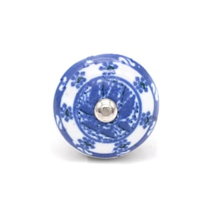Op de afbeelding: Een ronde, blauw-witte keramische kastknop met een zilveren metalen schroef. De knop heeft een bloemenpatroon in blauw tegen een witte achtergrond. De knop is een decoratief hardware-element.
