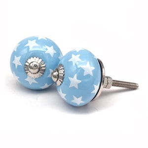Pair of hand-painted sky-blue ceramic cabinet knobs with white star motifs and metal threaded posts for drawers.
