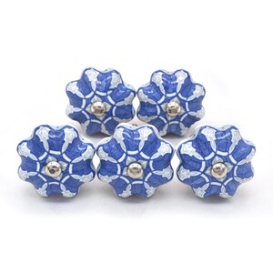Peut inclure: Cinq boutons de meuble en céramique bleus et blancs avec un motif floral. Chaque bouton a un centre argenté. Les boutons sont disposés en groupe, mettant en valeur leur motif décoratif et leur potentiel pour la décoration intérieure.