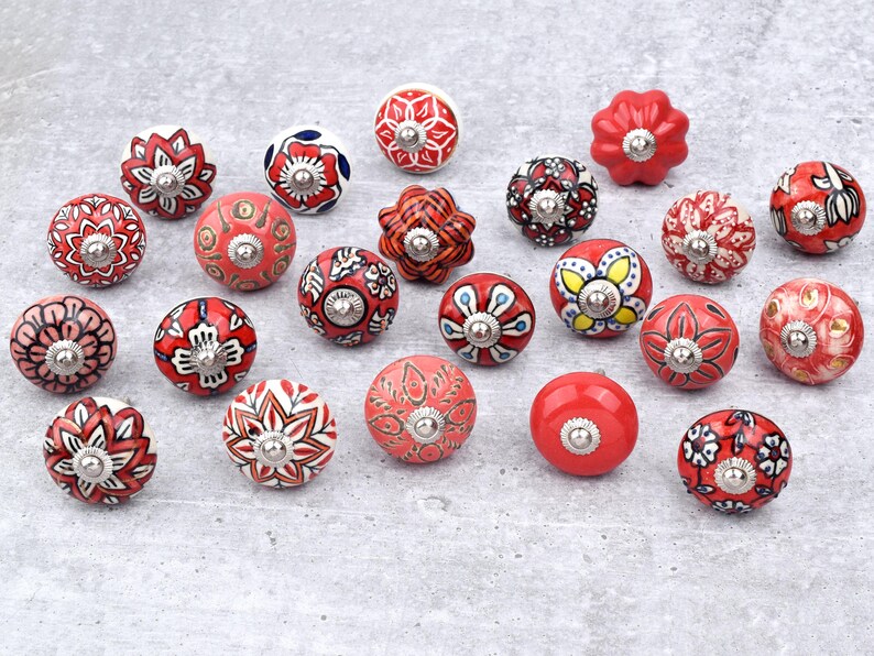 Red ceramic knobs with hand-painted white floral and mandala designs; assorted cabinet knobs for furniture and home décor.