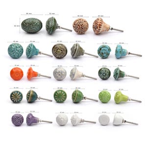May include: A collection of twelve decorative cabinet knobs in various colours and patterns. Each knob features a round or oval shape with a metal bolt extending from the back. The designs include floral, geometric, and solid textures in shades of green, blue, orange, purple, white, and grey.