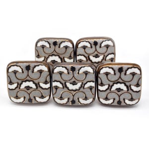 Może przedstawiać: Zestaw pięciu kwadratowych ceramicznych gałek do szafek z wzorem kwiatowym w kolorze szarym, czarnym i białym. Gałki mają brązowe wykończenie.