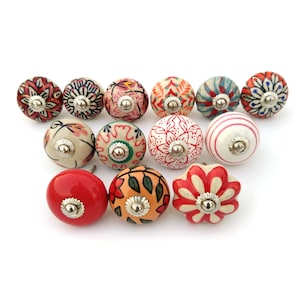 以下が含まれることがあります： 装飾的なセラミックキャビネットノブのコレクション。ノブは、花柄、ストライプ、単色など、さまざまなパターンと色を特徴としています。各ノブには、銀色の金属ベースが付いています。