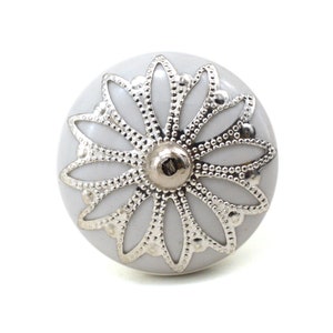 White ceramic cabinet knob with a silver flower motif and gold center; decorative furniture knob for cabinets and drawers.