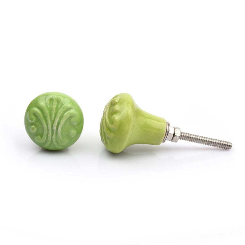 May include: A collection of twelve decorative cabinet knobs in various colours and patterns. Each knob features a round or oval shape with a metal bolt extending from the back. The designs include floral, geometric, and solid textures in shades of green, blue, orange, purple, white, and grey.