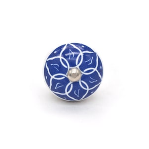May include: A round cabinet knob with a white base and a blue floral design. The design features interconnected white lines on a blue background. A silver-coloured screw is in the centre.