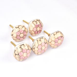 Op de afbeelding: Een set van vijf decoratieve kastknoppen. Elke knop heeft een zeshoekig patroon in roze en goud, met een messing steel. De knoppen zijn ontworpen voor meubels en woondecoratie. Diameter ongeveer 3 cm.