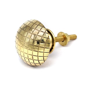 May include: A gold-toned cabinet knob with a square patterned design. The knob has a screw-on attachment.
