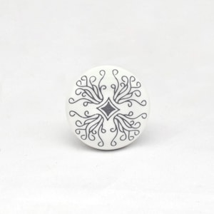 Op de afbeelding: Witte keramische kastknop met een grijs, symmetrisch, wervelend ontwerp. Het ontwerp heeft een centrale ruitvorm en krullende lijnen. Geschikt voor laden en kasten.