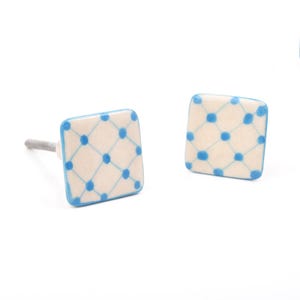 May include: Two square cabinet knobs with a cream-colored background and a blue lattice pattern. The edges are outlined in blue. One knob has a silver-colored stem.