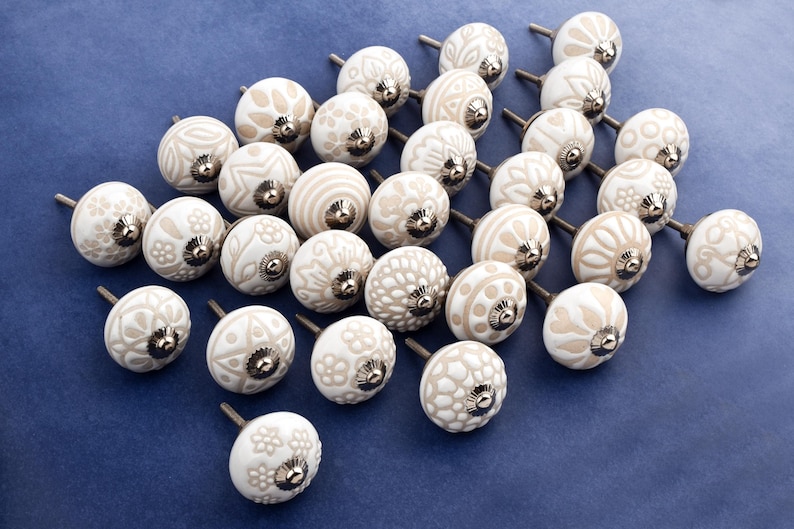 collection of white ceramic drawer knobs with intricate floral patterns and silver accents. The knobs are arranged in a basket lined with peach-colored fabric.