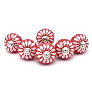 Può includere: Sei pomelli in ceramica rossa con motivi floreali bianchi. I pomelli hanno una base in metallo argentato.