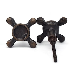 Peut inclure: Deux boutons de meuble de style antique avec un design en forme de croix. Les boutons sont en métal et ont une finition brun foncé. Un bouton a une vis pour le fixer à une surface.