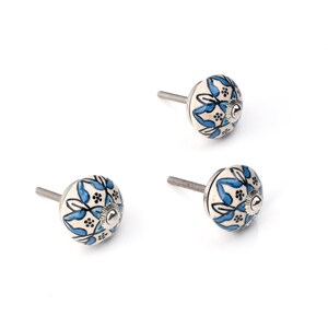 Assorted hand-painted ceramic knobs in blue, black and white with mandala and floral motifs for cupboard handles and kitchen decor.