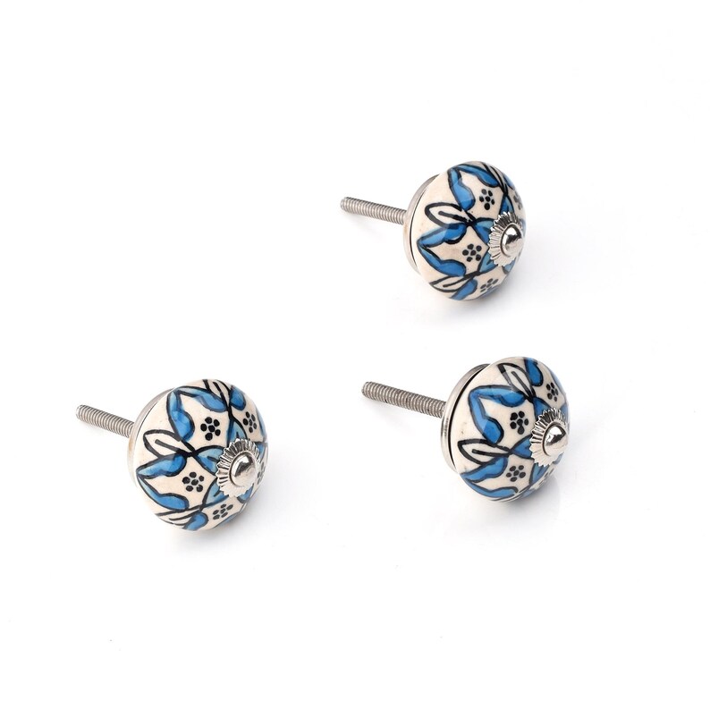 Assorted hand-painted ceramic knobs in blue, black and white with mandala and floral motifs for cupboard handles and kitchen decor.