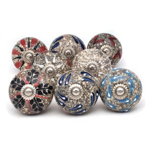 Peut inclure: Un ensemble de neuf boutons de cabinet en céramique avec une base grise mouchetée et divers motifs colorés. Les boutons ont une base en métal argenté.
